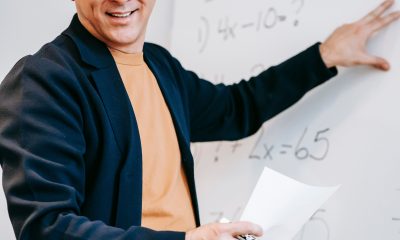 A teacher smiling beside a whiteboard during a maths lesson