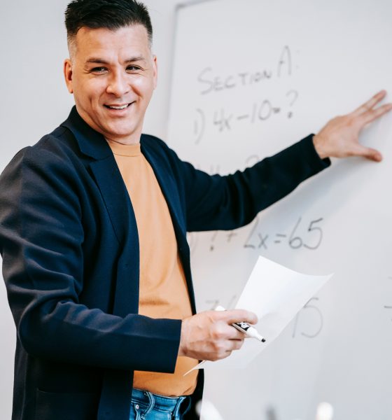 A teacher smiling beside a whiteboard during a maths lesson