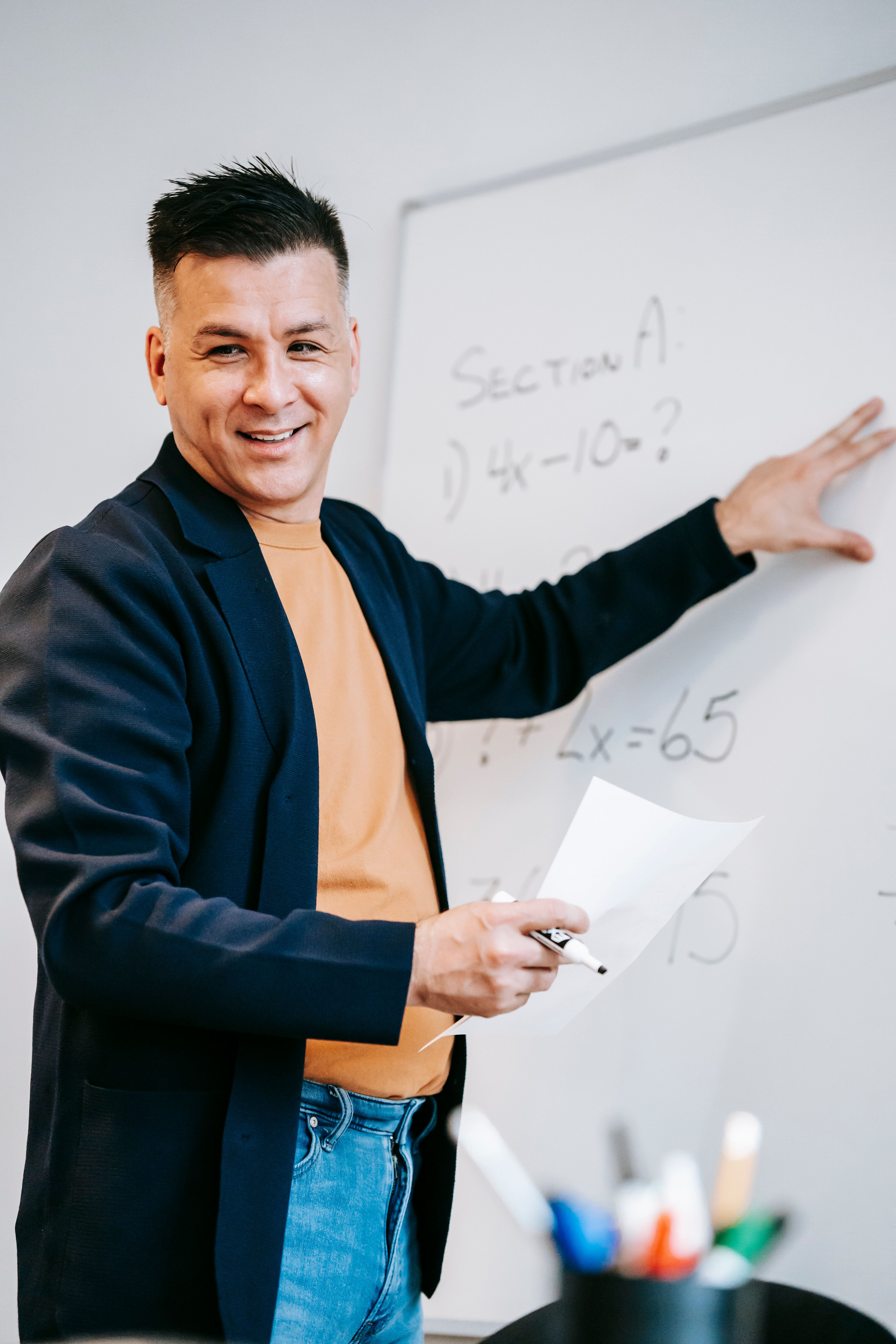 A teacher smiling beside a whiteboard during a maths lesson